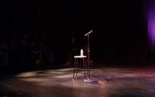 Leere Open-Mic-Bühne mit Mikrofon, Hocker und Wasserflasche im Scheinwerferlicht