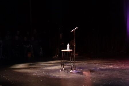 Leere Open-Mic-Bühne mit Mikrofon, Hocker und Wasserflasche im Scheinwerferlicht