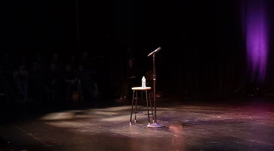 Leere Open-Mic-Bühne mit Mikrofon, Hocker und Wasserflasche im Scheinwerferlicht