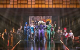 Bunt beleuchtete Theaterbühne mit Ensemble in verschiedenen Kostümen