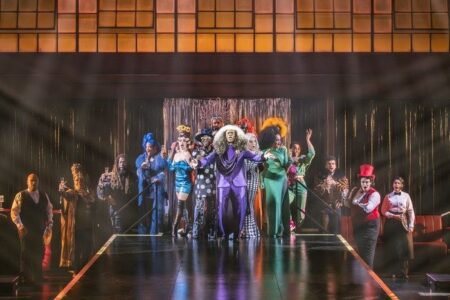 Bunt beleuchtete Theaterbühne mit Ensemble in verschiedenen Kostümen