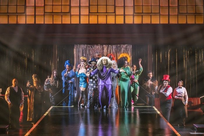 Bunt beleuchtete Theaterbühne mit Ensemble in verschiedenen Kostümen